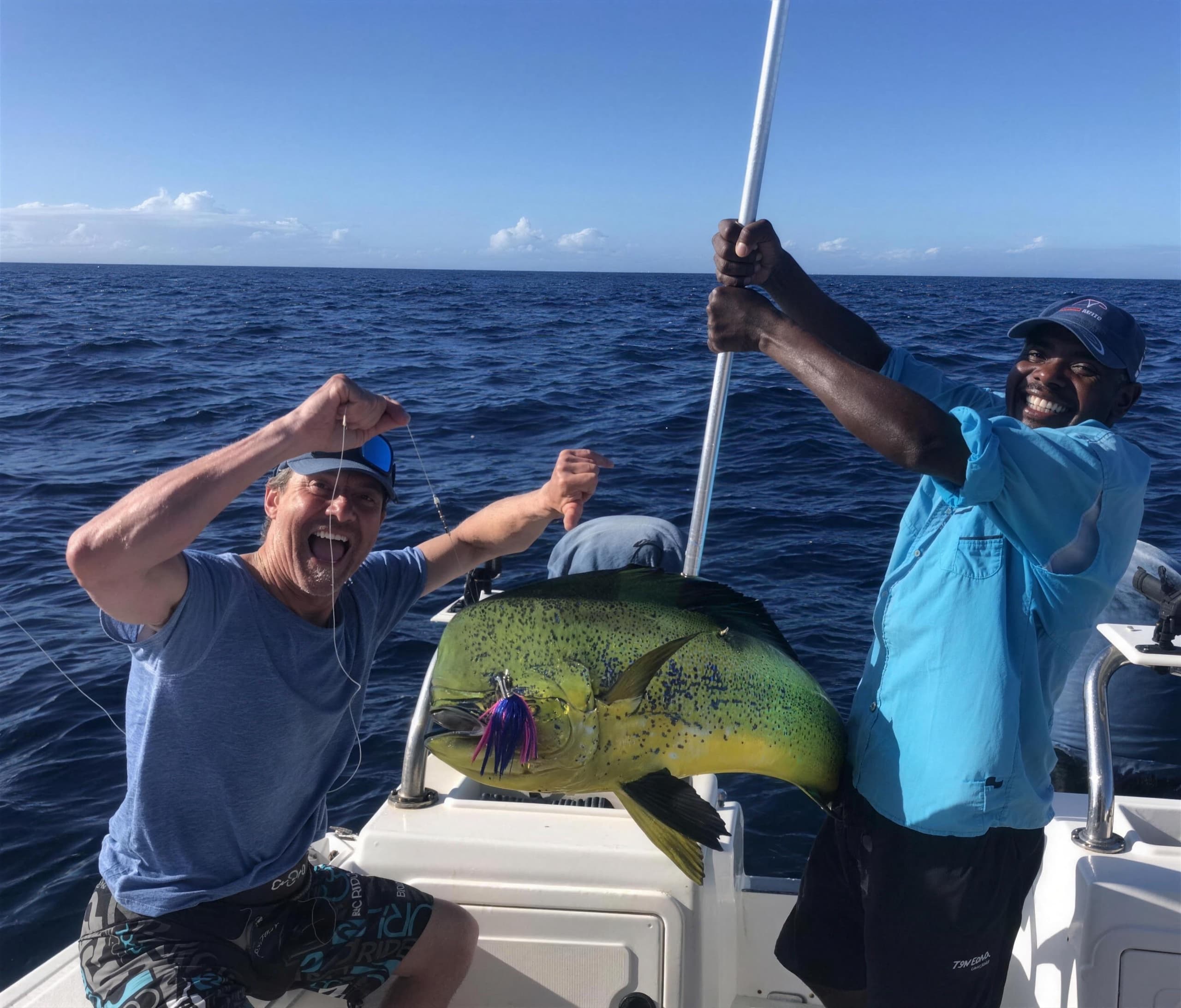 Two anglers celebrating a mahi-mahi at the rail of the boat on open blue water